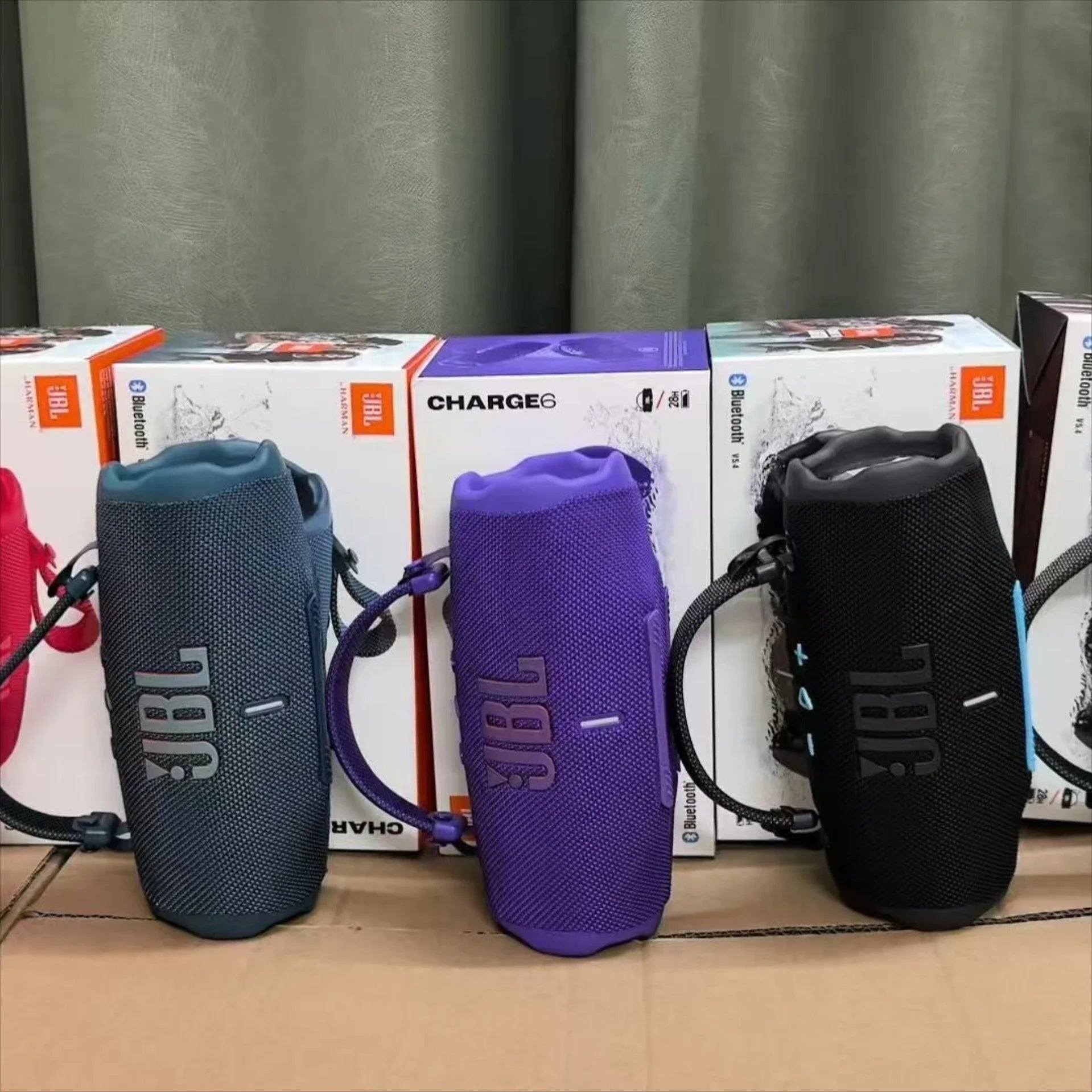 Three JBL speakers in blue, purple, and black on top of their packaging boxes.